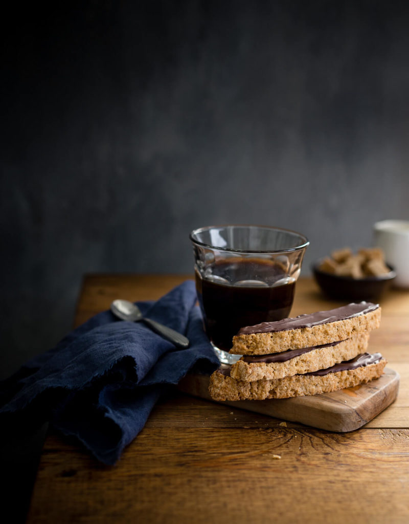 Almond biscotti and a cup of coffee on a small wooden board with a blue napkin.