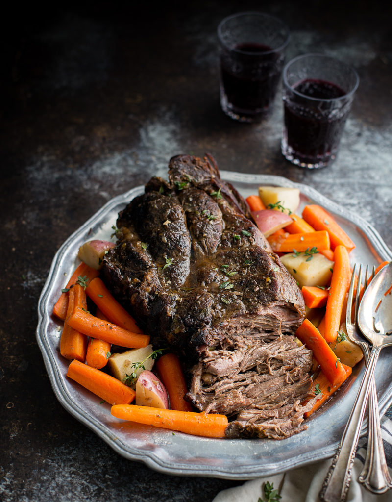 A pot roast on a serving platter with carrots and potatoes.