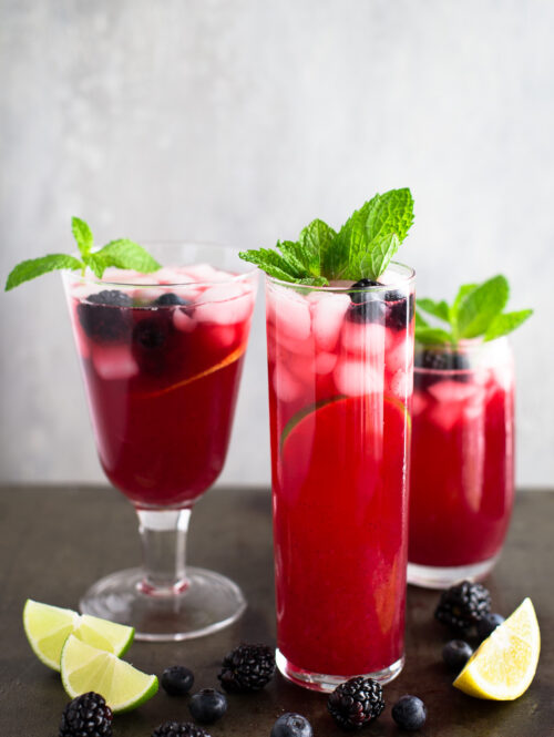Three glasses of blackberry-blueberry lemonade garnished with mint sprigs.