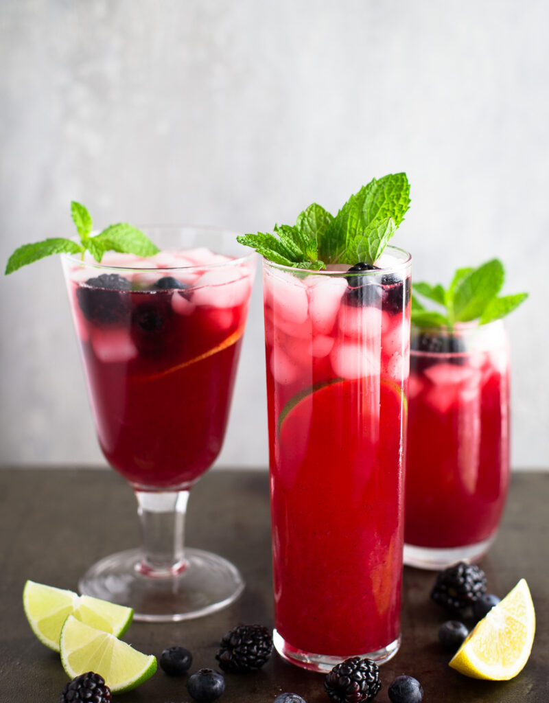 Three glasses of blackberry-blueberry lemonade garnished with mint sprigs.
