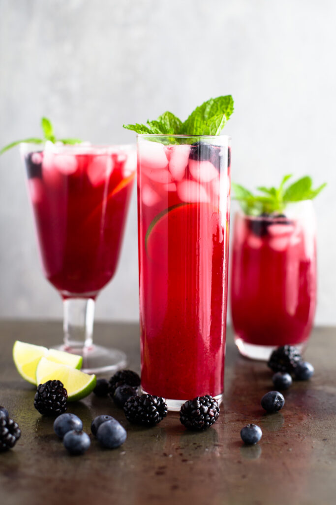 Three glasses of blackberry-blueberry lemonade garnished with mint sprigs.