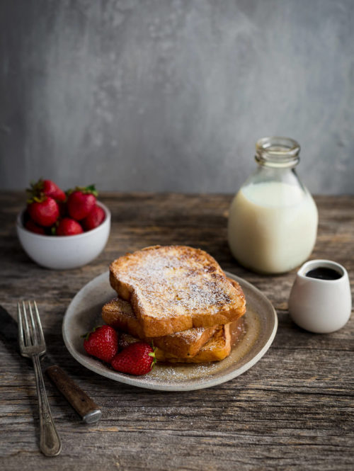 Slices of french toast dusted with powdered sugar served with strawberries.