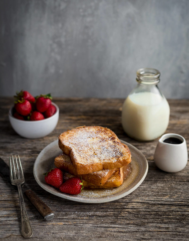 Slices of french toast dusted with powdered sugar served with strawberries.