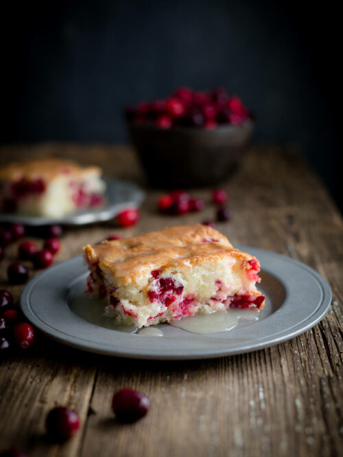 Serving of cranberry pudding cake topped with warm butter sauce on a pewter plate on wooden background.