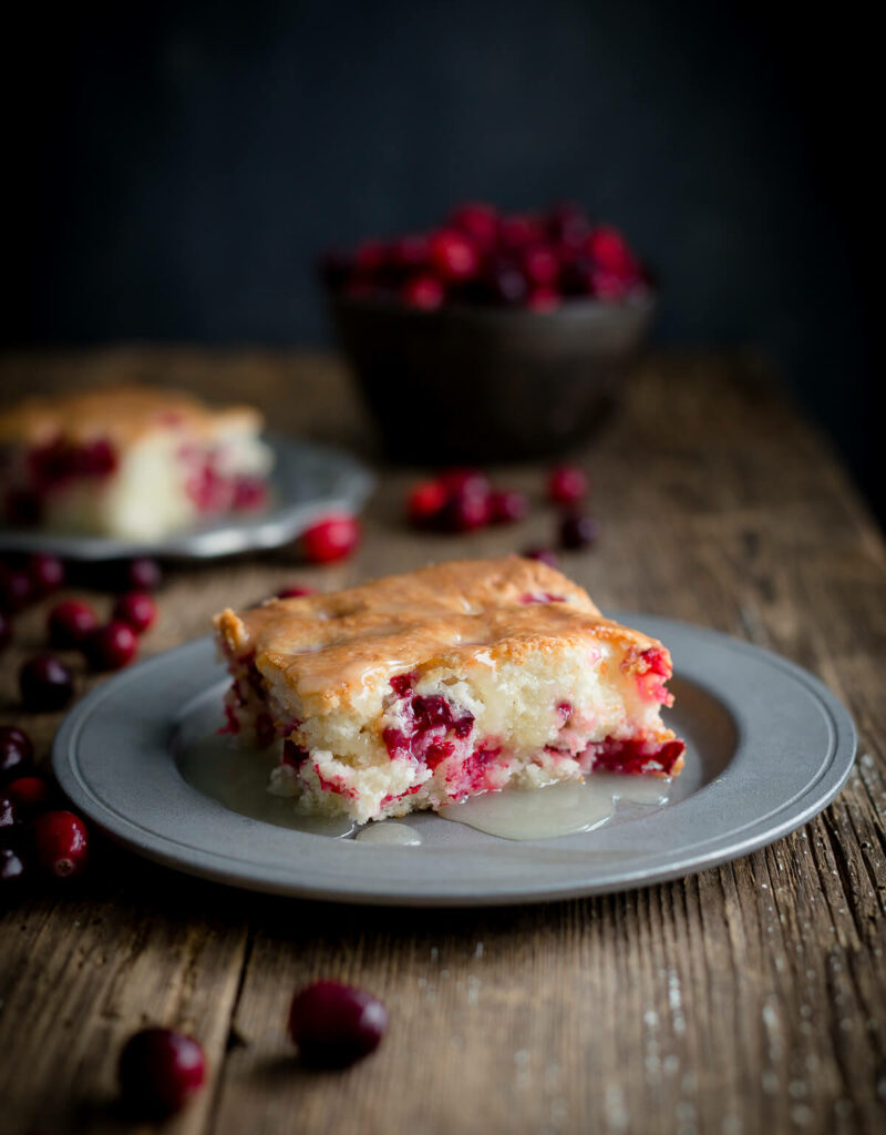 Serving of cranberry pudding cake topped with warm butter sauce on a pewter plate on wooden background.
