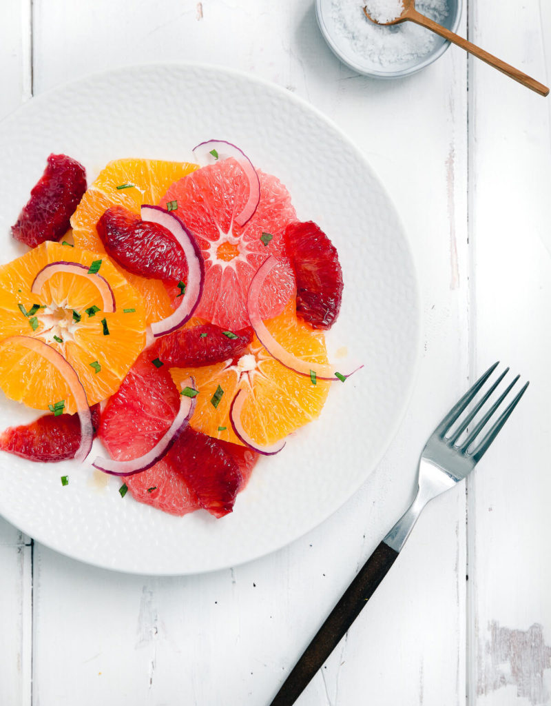 Overhead shot of a citrus salad with grapefruit, blood oranges, and navel oranges on a white plate.