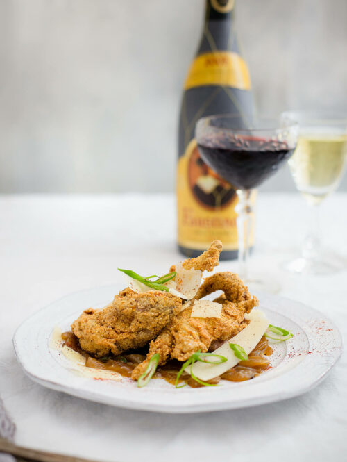 Fried quail on a white plate next to two glasses of wine.