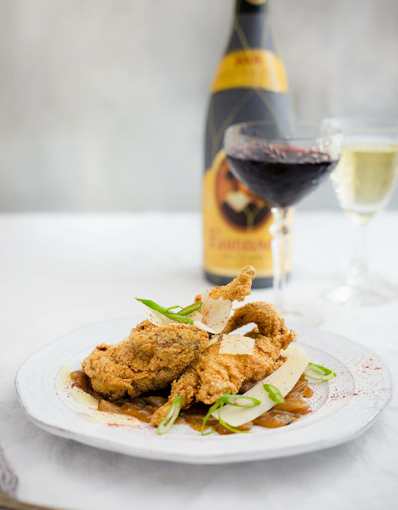 Fried quail on a white plate next to two glasses of wine.