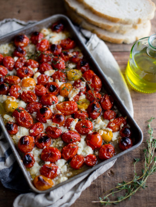 A baking tray of roasted tomatoes and feta topped with olive oil and thyme.