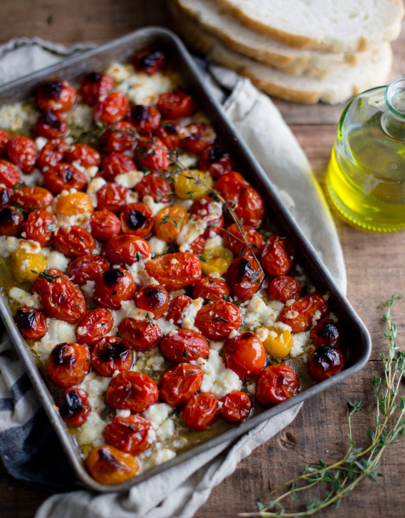 A baking tray of roasted tomatoes and feta topped with olive oil and thyme.