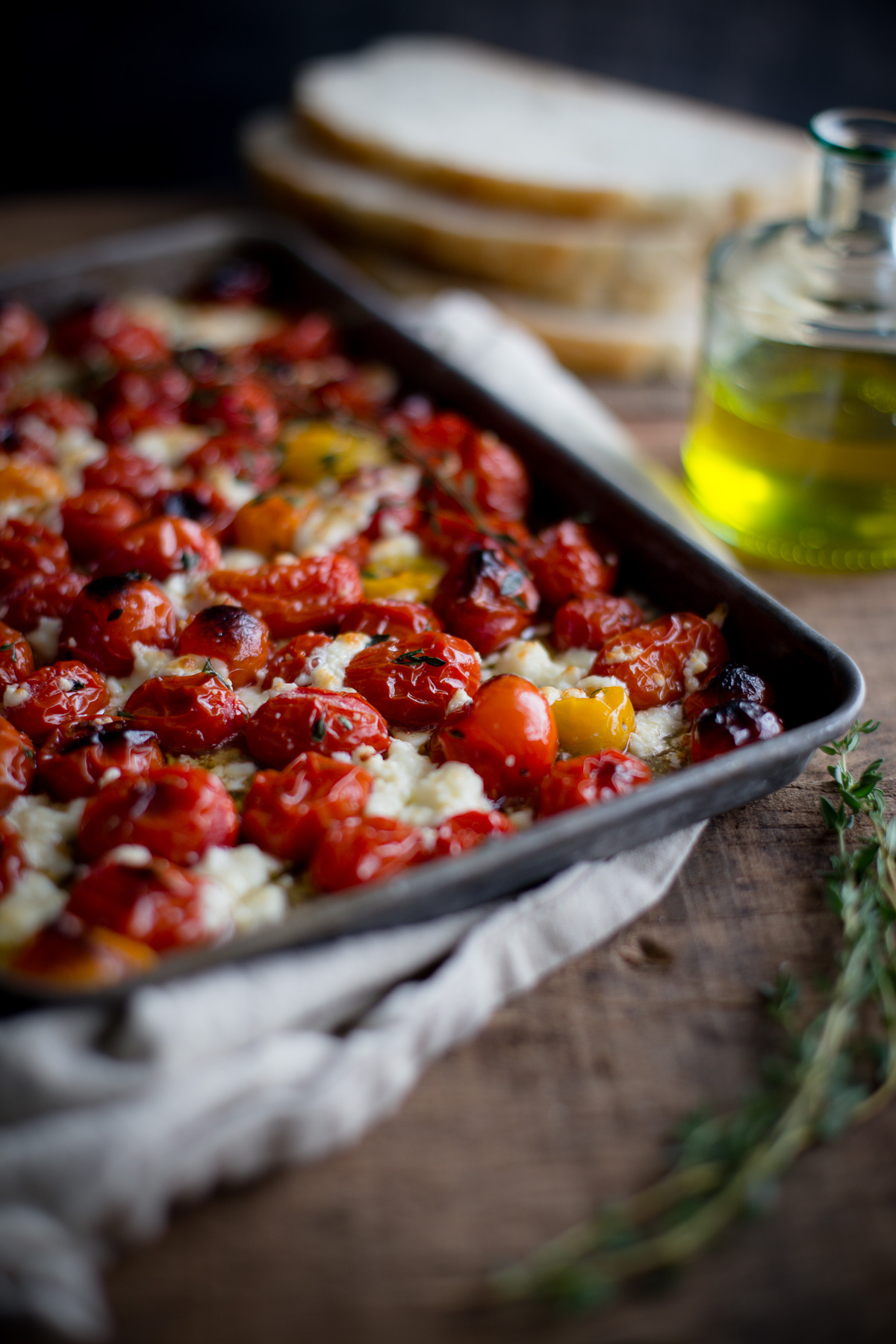 A baking tray of roasted tomatoes and feta topped with olive oil and thyme.