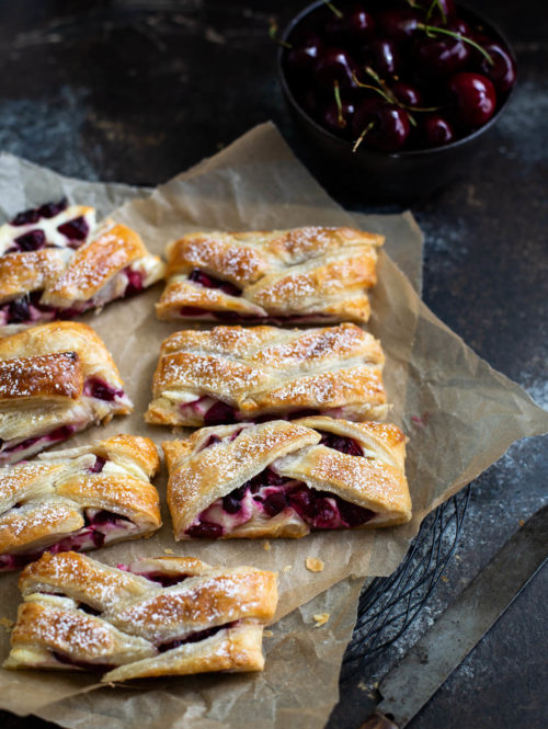 Several slices of cherry cream cheese danish on brown parchment paper.