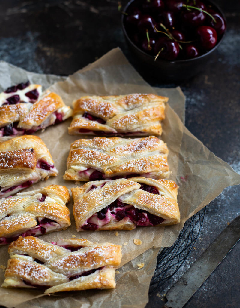 Several slices of cherry cream cheese danish on brown parchment paper.