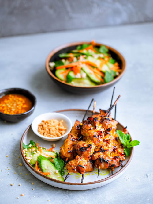Skewers of chicken satay served with a cucumber salad.