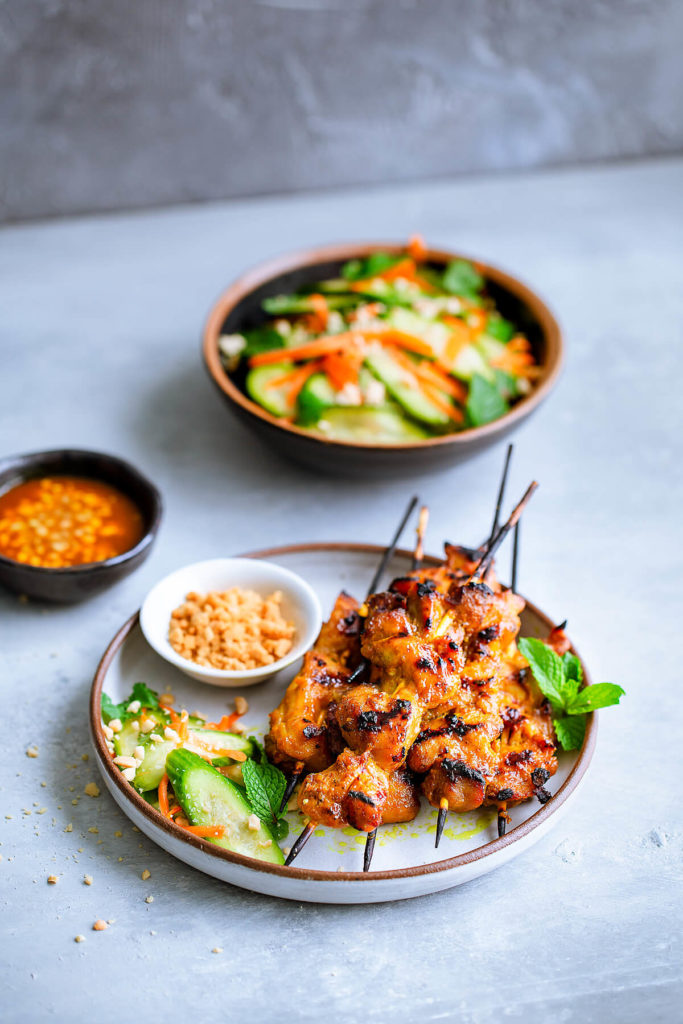 Skewers of chicken satay served with a cucumber salad.