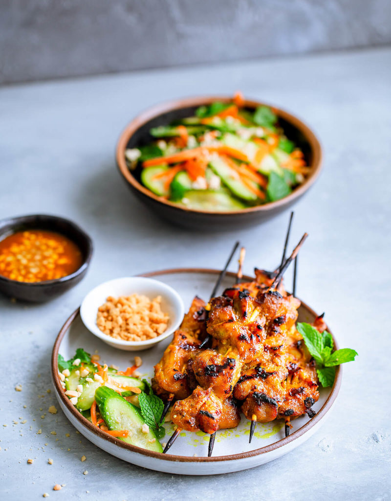 Skewers of chicken satay served with a cucumber salad.