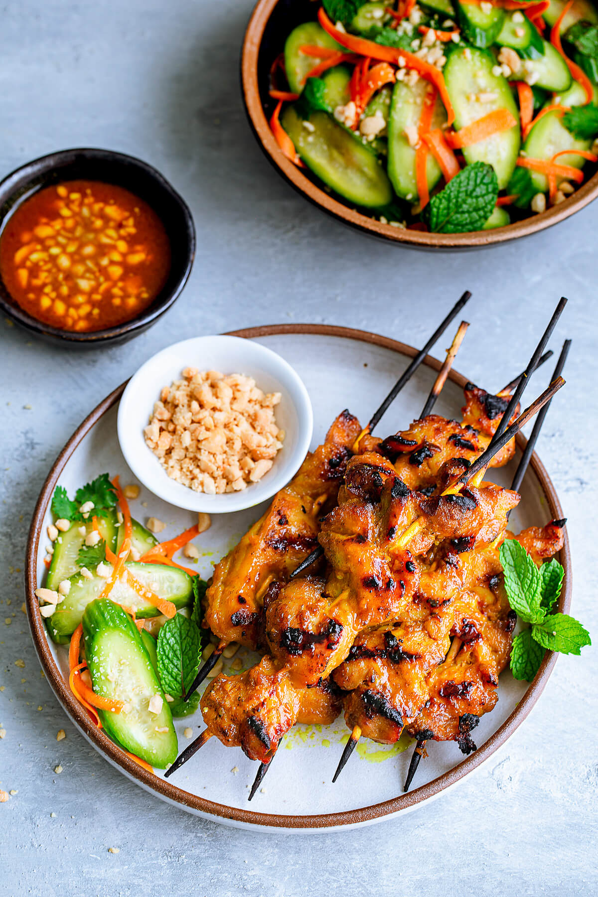 Overhead view of skewers of chicken satay served with a cucumber salad.