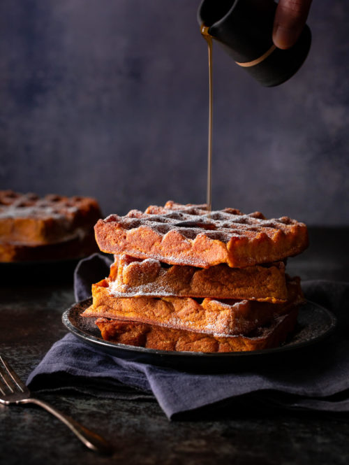 Syrup being poured on a stack of pumpkin spice waffles.