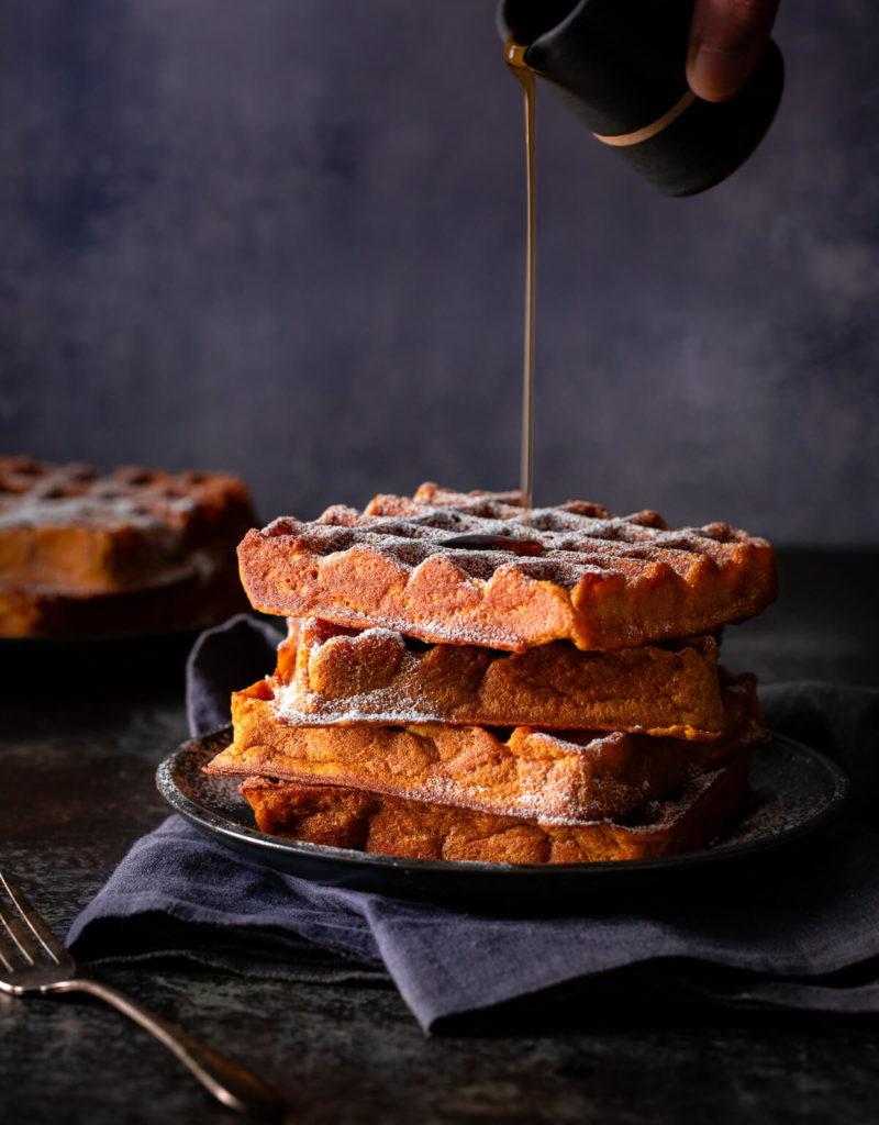 Syrup being poured on a stack of pumpkin spice waffles.