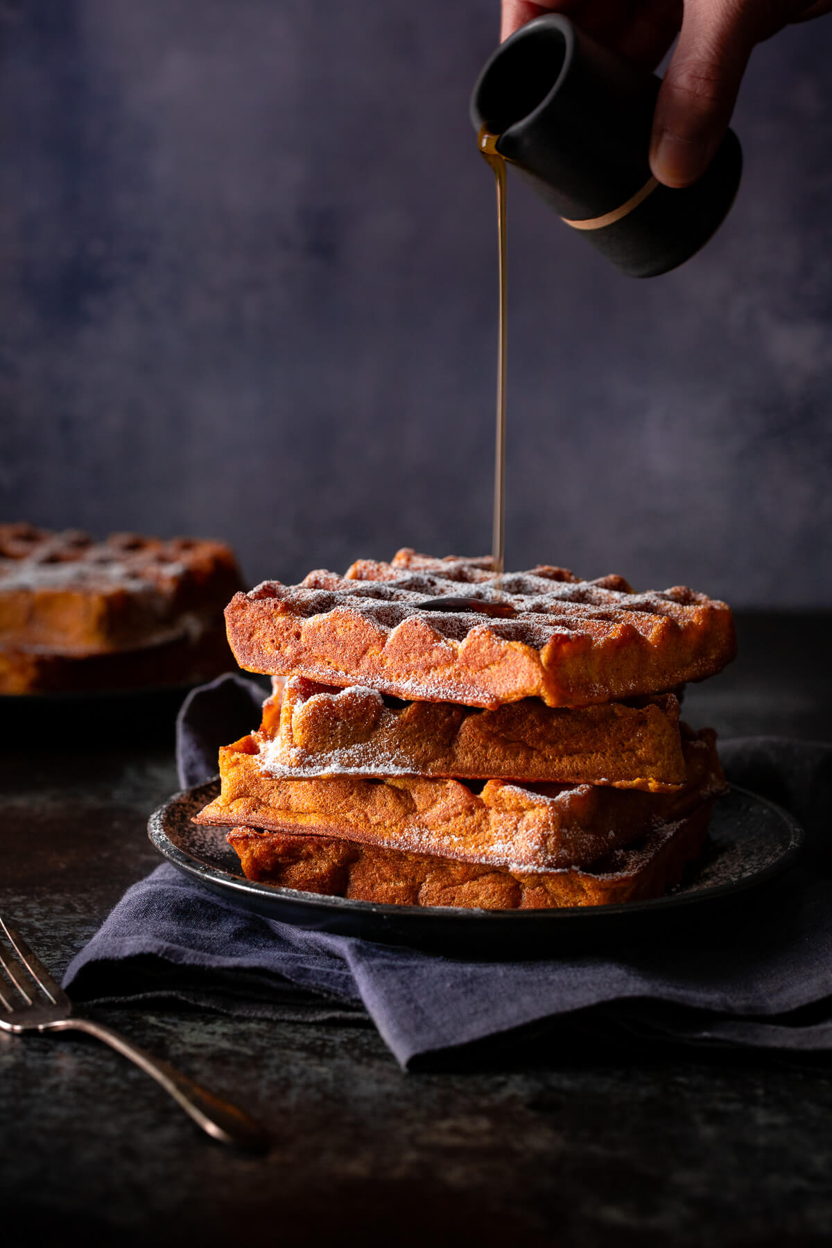 Syrup being poured on a stack of pumpkin spice waffles.