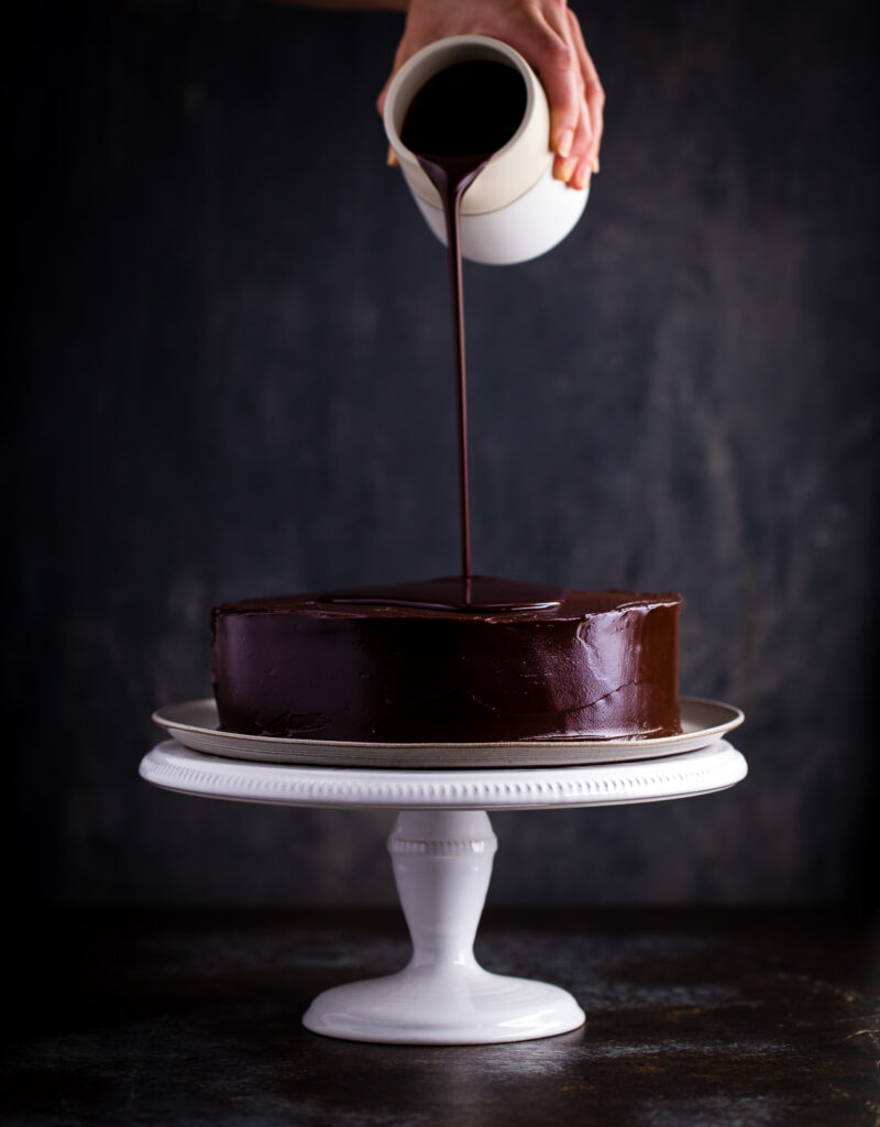 Chocolate ganache being poured on an inside-out German chocolate cake.