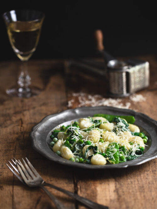 A plate of lemon gnocchi with spinach and peas on a wooden tabletop.