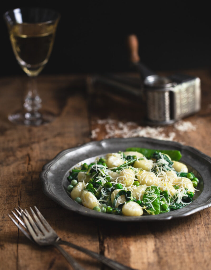 A plate of lemon gnocchi with spinach and peas on a wooden tabletop.