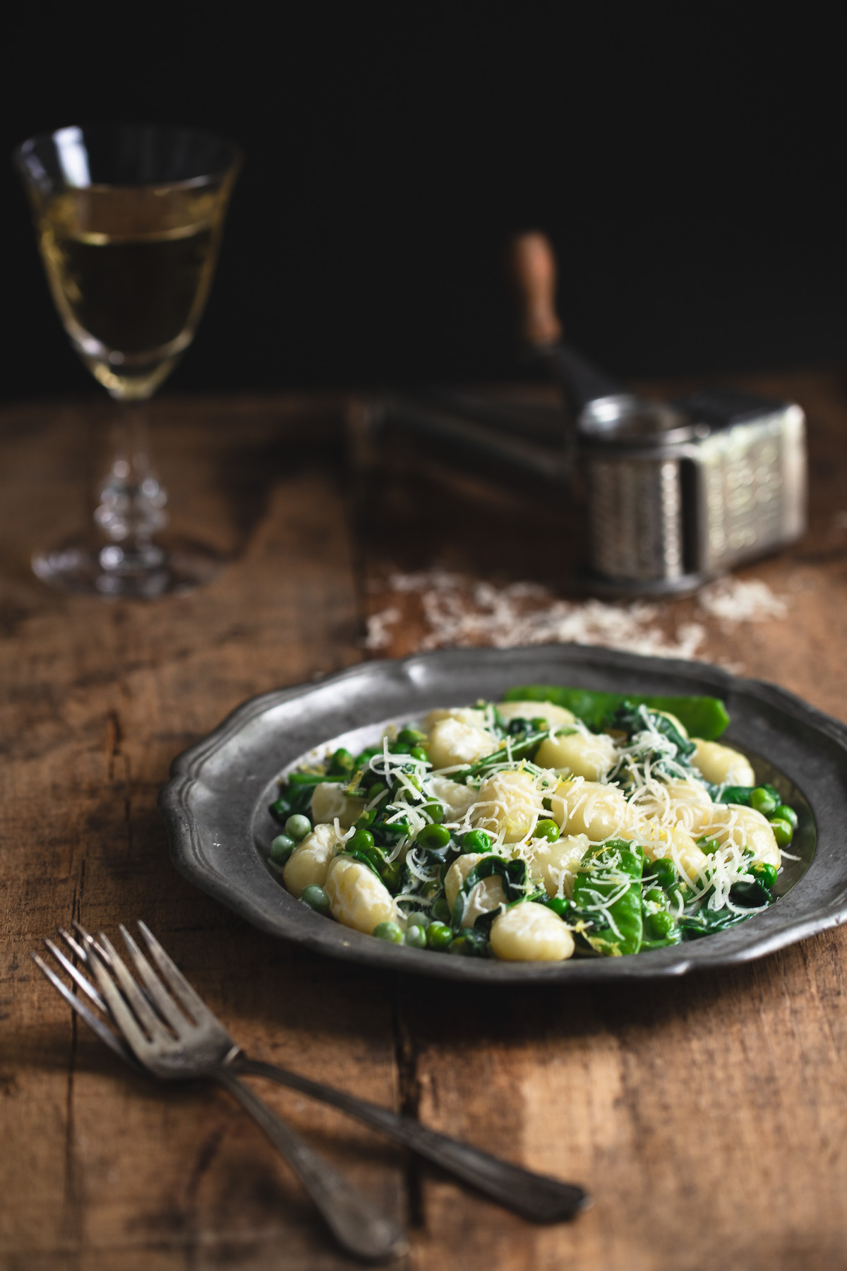 A plate of lemon gnocchi with spinach and peas on a wooden tabletop.