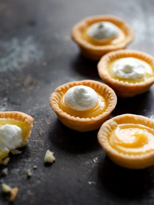 Close-up of several lemon tartlets topped with whipped cream on a tabletop.