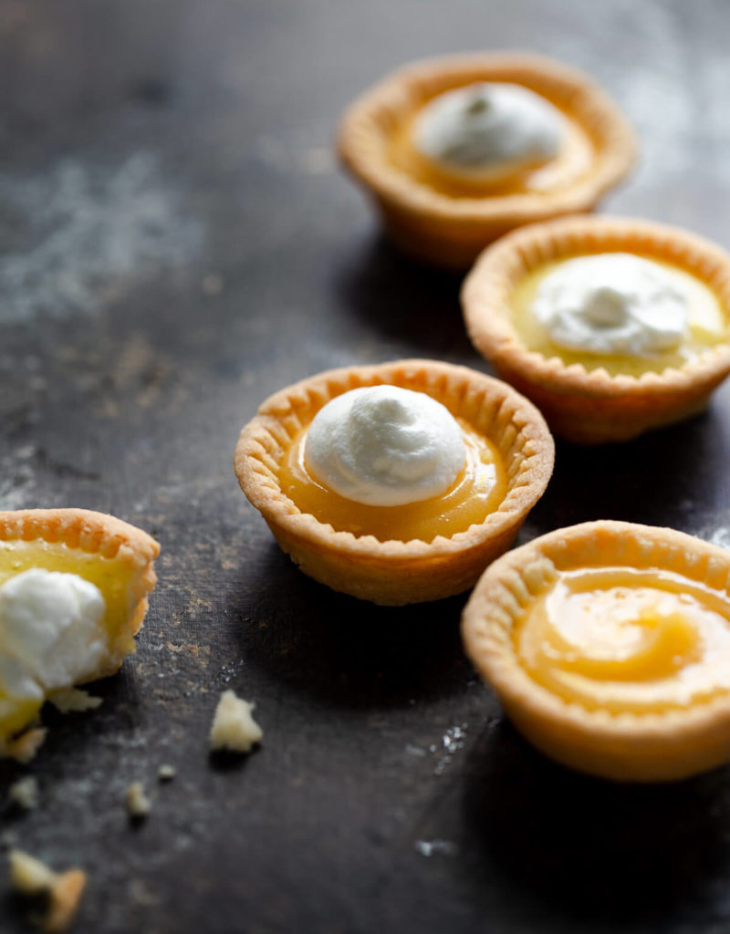 Close-up of several lemon tartlets topped with whipped cream on a tabletop.