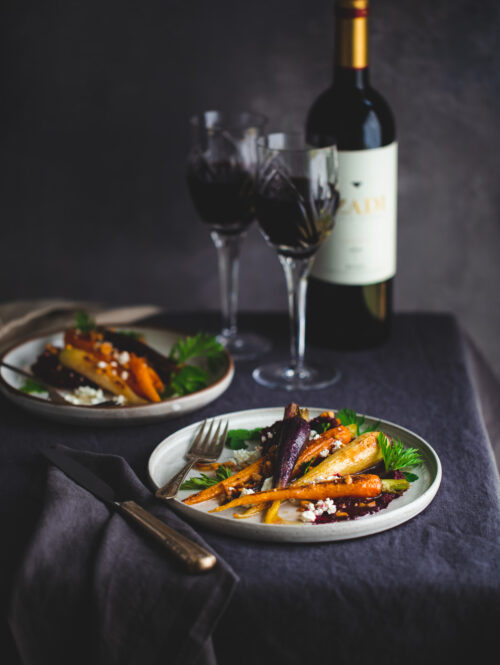 Plates of roasted carrots with beet purée next to wine glasses.