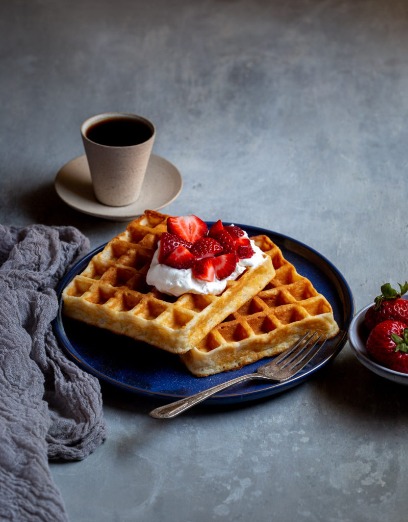 Two Belgian waffles topped with whipped cream and strawberries on a blue plate.