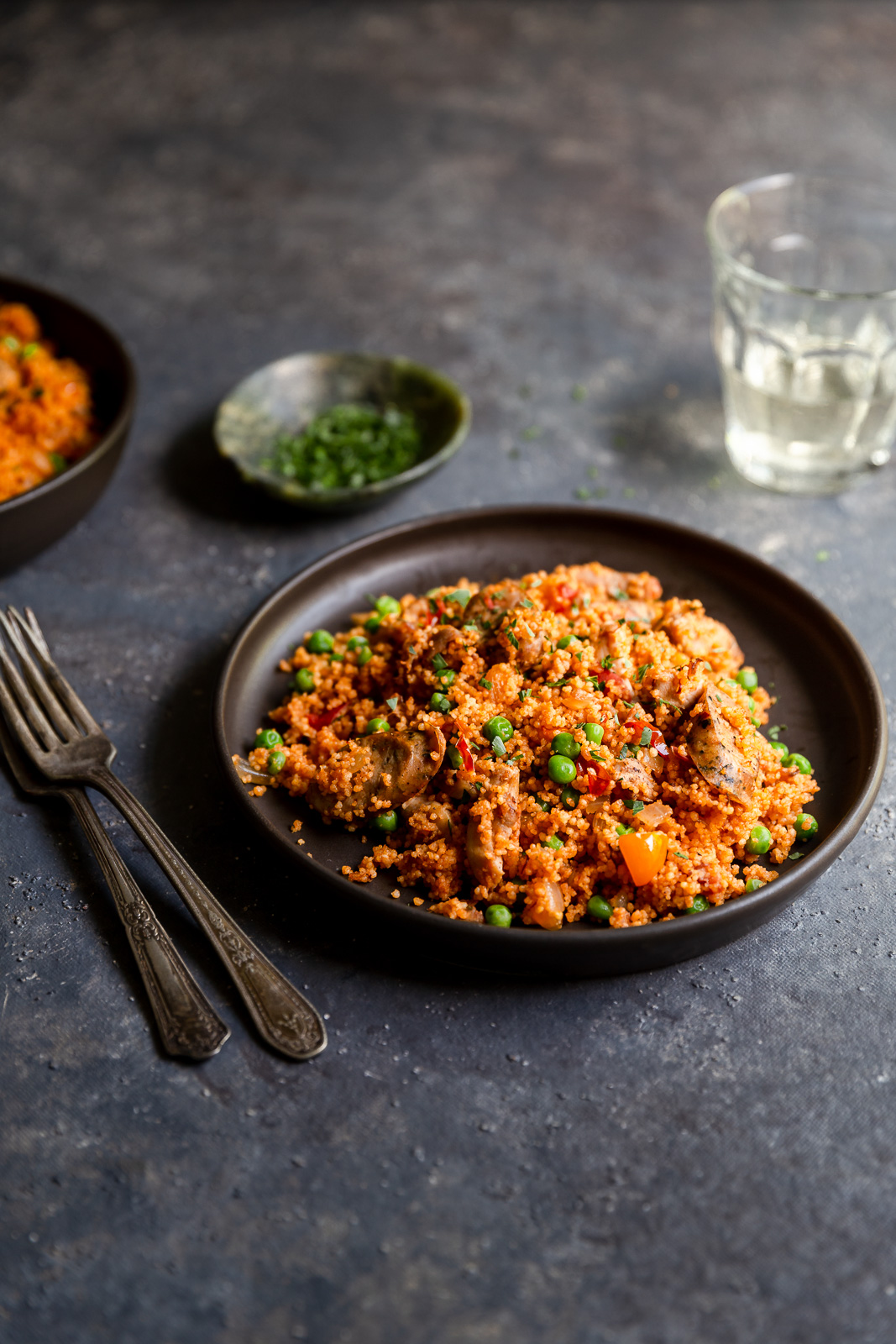 Chicken and sausage couscous paella  on a brown plate with a glass of white wine and some chopped parsley.