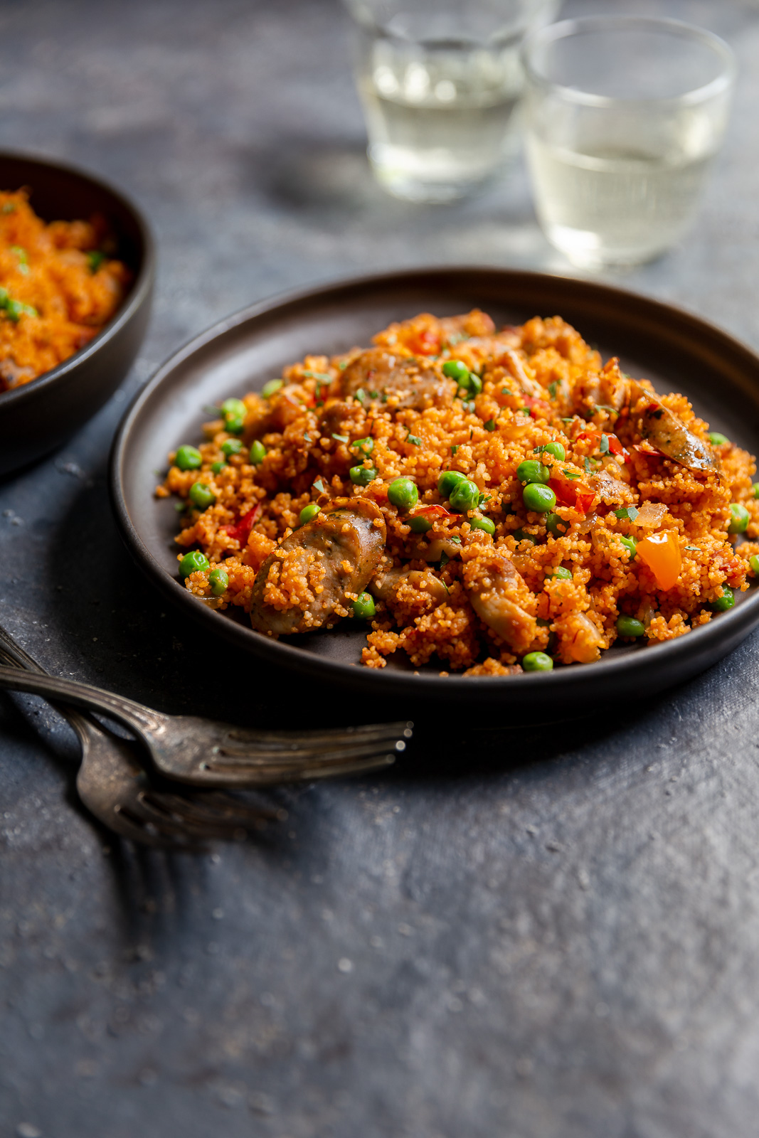 Chicken and sausage couscous paella  on a brown plate with glasses of white wine.