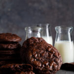 Stack of dark chocolate cookies shown with small bottles of milk.