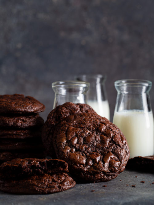 Stack of dark chocolate cookies shown with small bottles of milk.