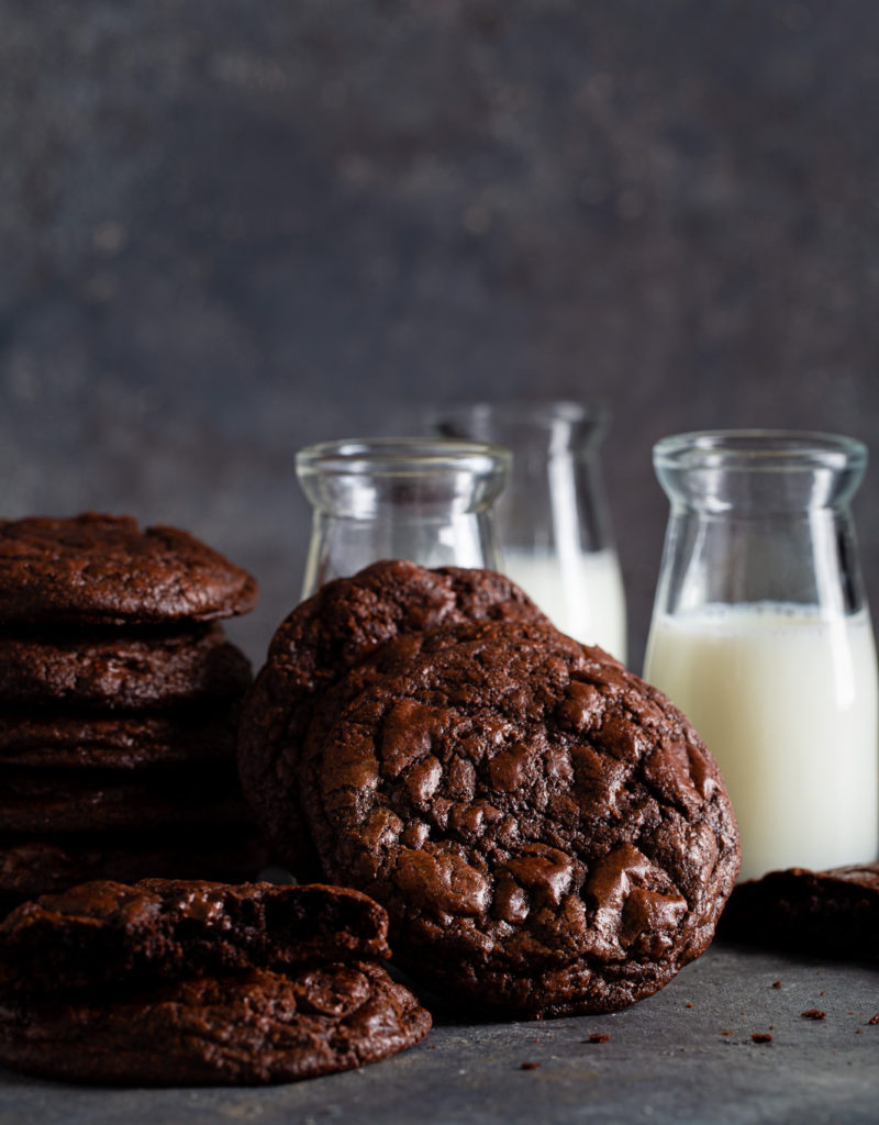 Stack of dark chocolate cookies shown with small bottles of milk.