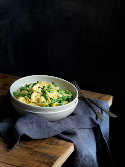 A stack of white bowls with some tortellini carbonara on a wooden table.