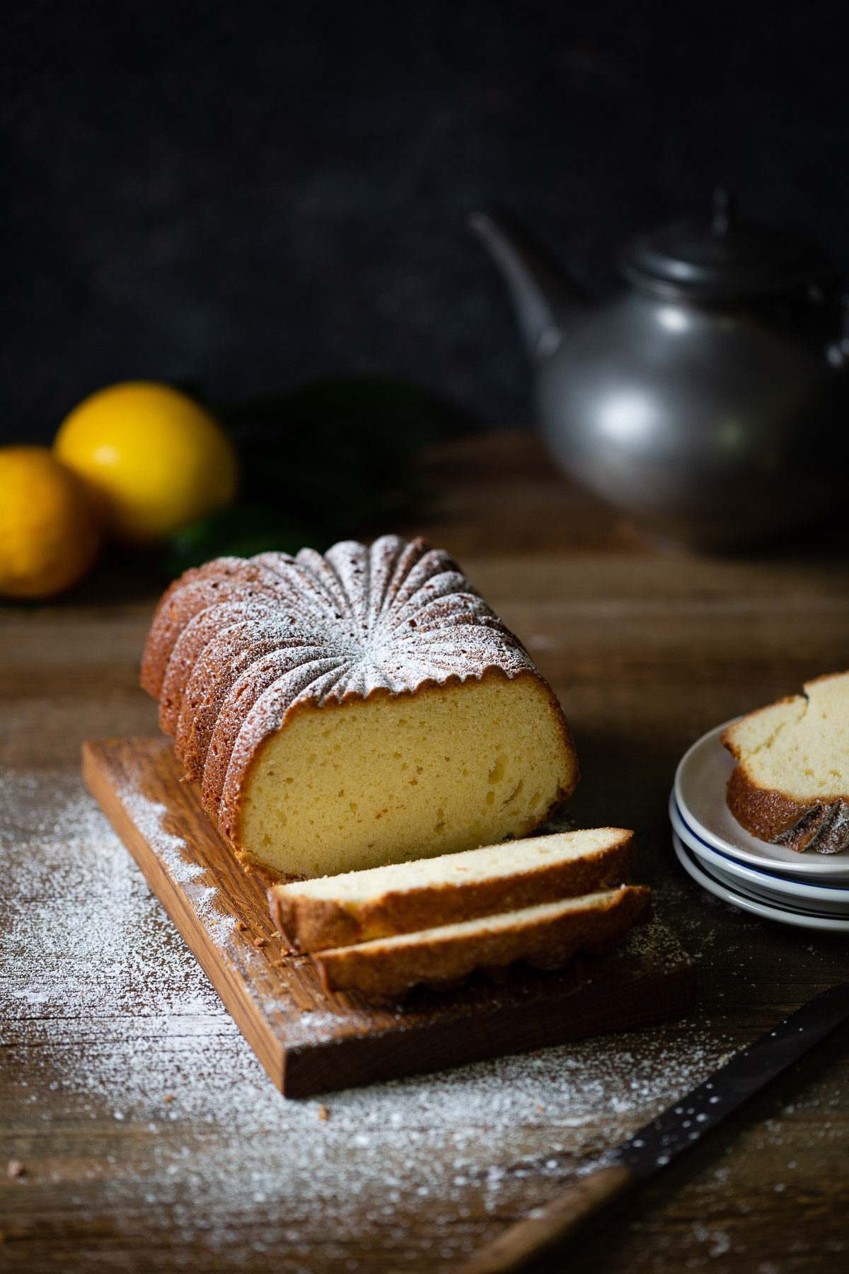 A lemon tea cake loaf with two slices cut and sprinkled with powdered sugar.