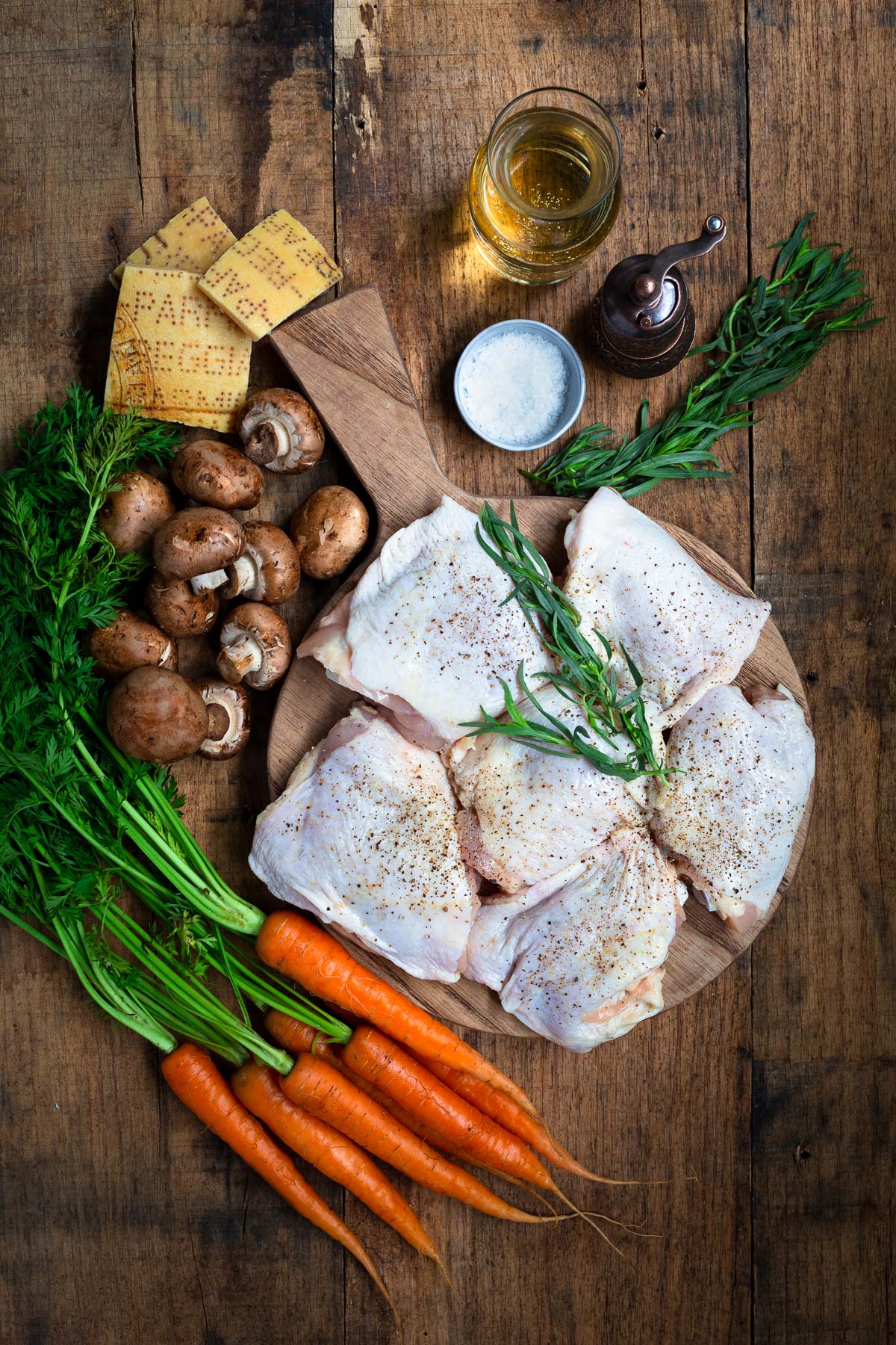 Ingredients for Creamy Chicken in White Wine Sauce set out on a wooden board - chicken, white wine, fresh carrots, mushrooms, tarragon, and Parmesan cheese rinds.