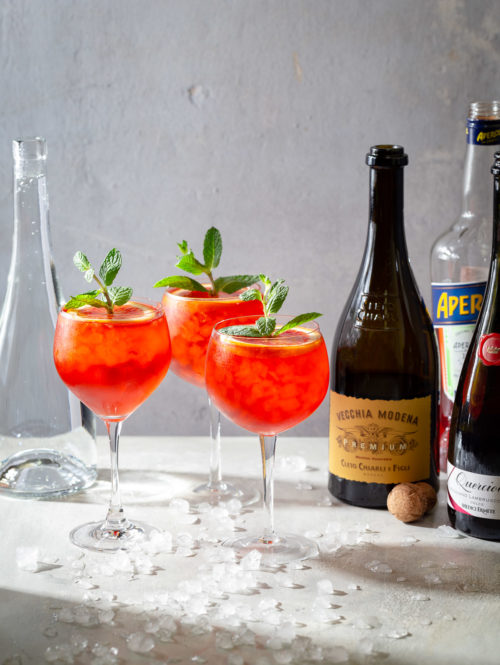 Three Lambrusco spritz cocktails garnished with orange slices and mint sprigs.