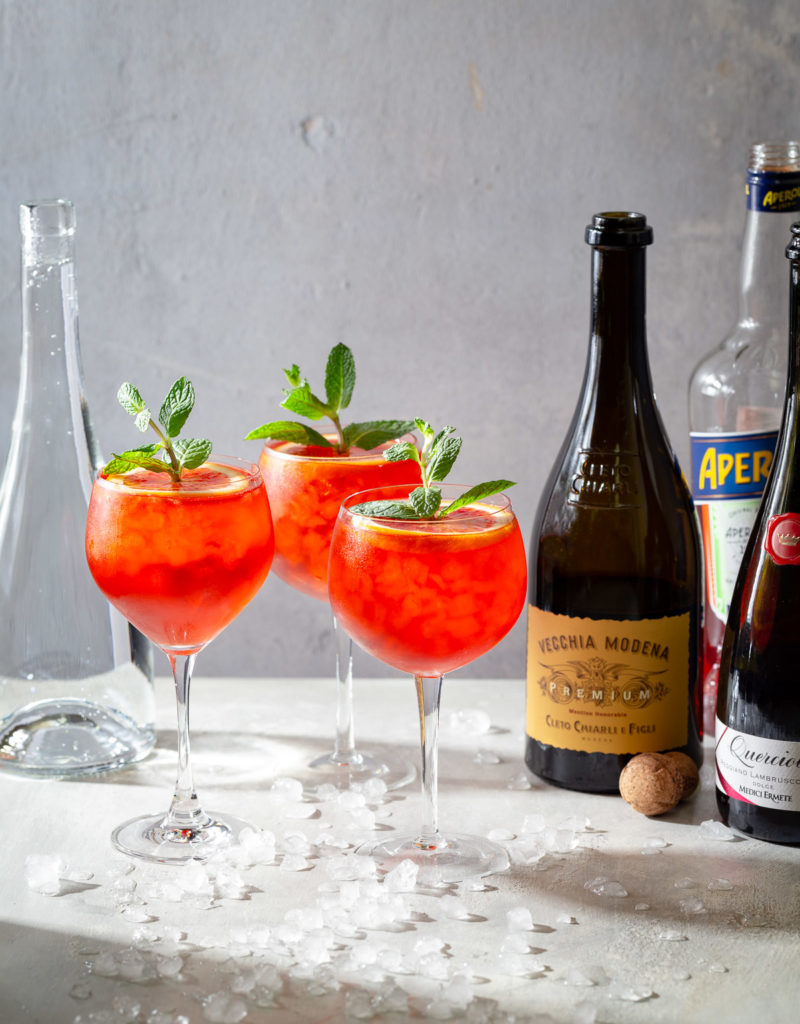 Three Lambrusco spritz cocktails garnished with orange slices and mint sprigs.
