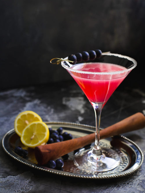 Blueberry Lemon Drop cocktail in a tall martini glass garnished with blueberries on a metal tray.