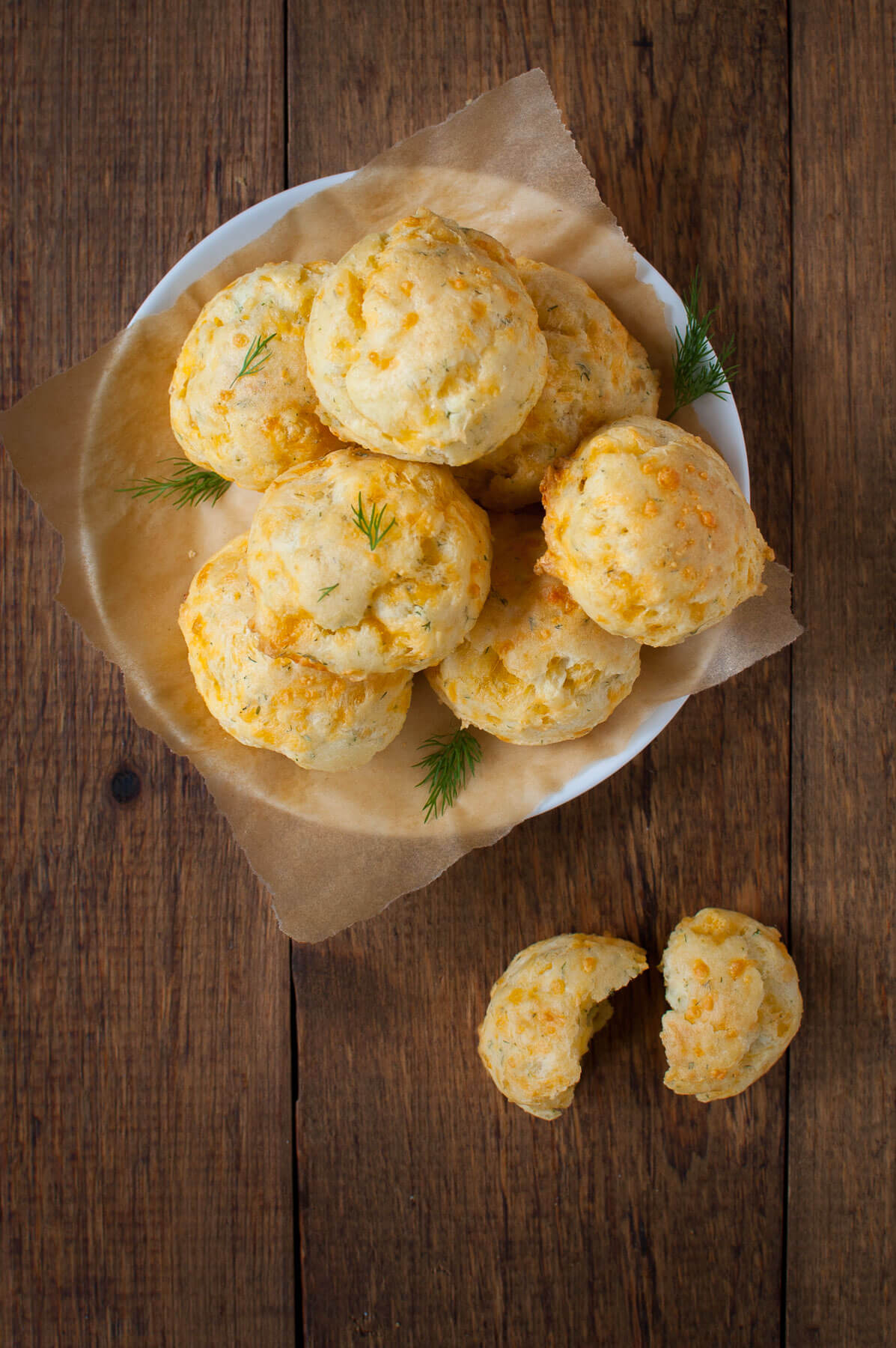 Overhead view of plate of cheddar dill puffs on a wooden background.