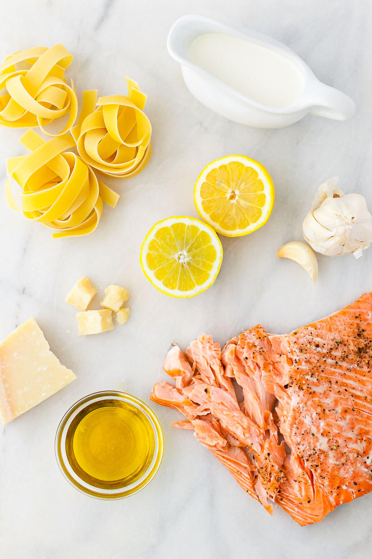 Ingredients for lemon pasta with salmon - dried pappardelle, cream, parmesan cheese, lemon, garlic, olive oil, and roasted salmon.