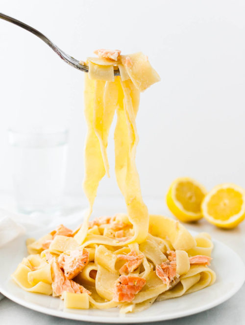 Lemon pasta with salmon twirled on a fork above a plate.