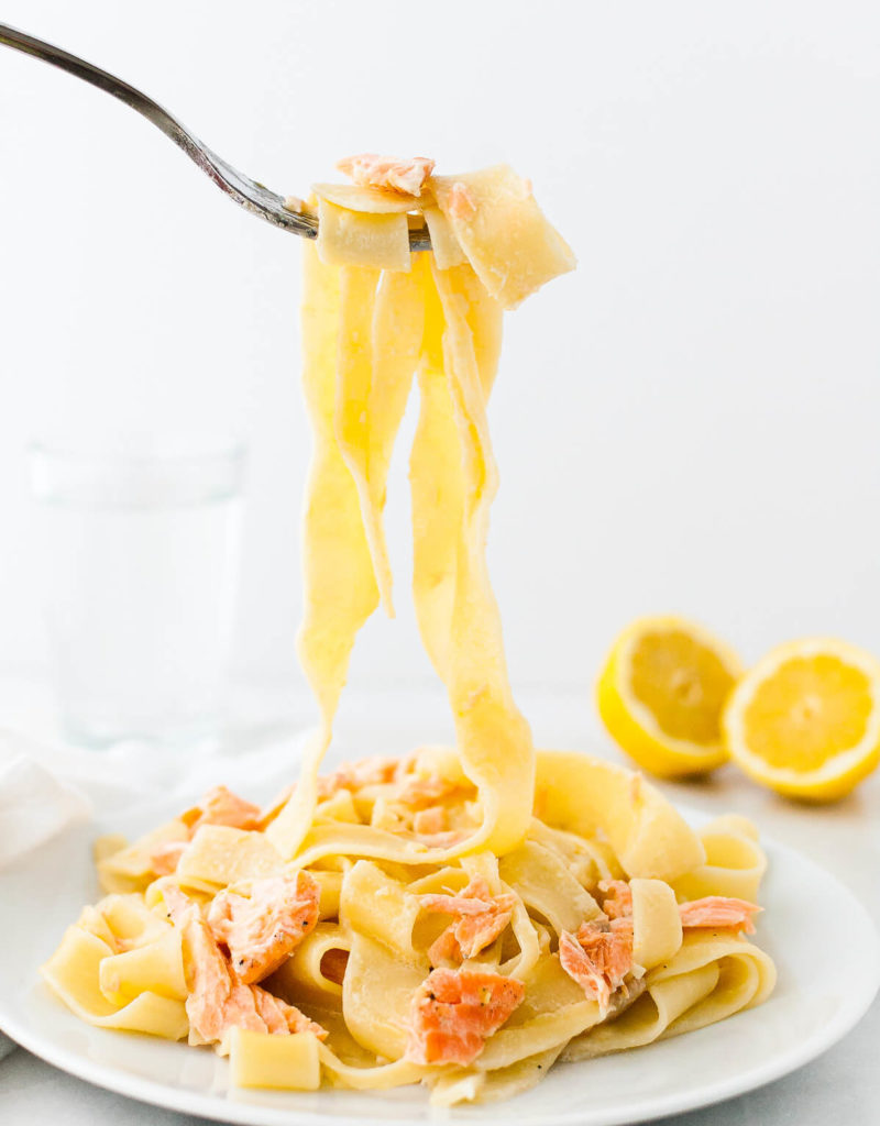 Lemon pasta with salmon twirled on a fork above a plate.