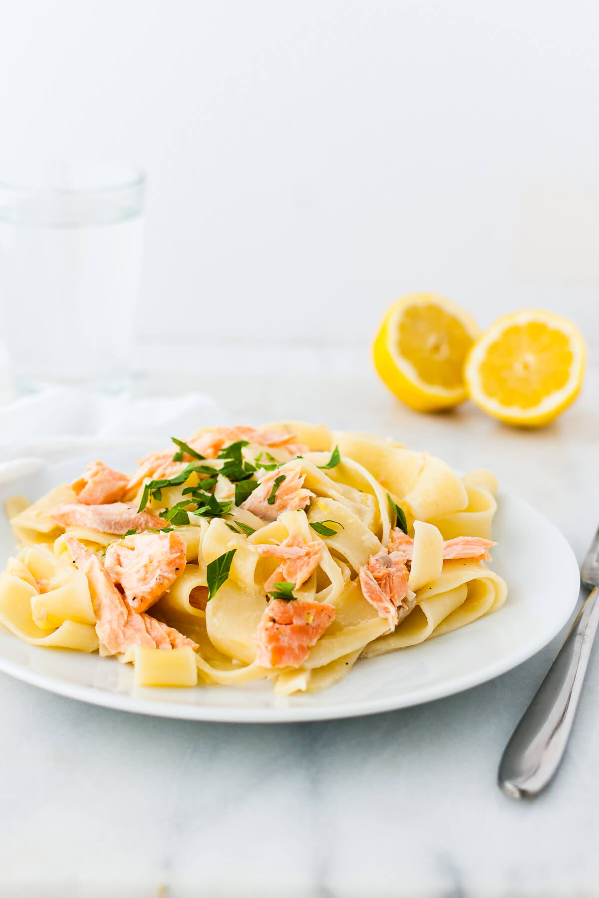 Lemon pasta with salmon garnished with chopped parsley on a white plate.