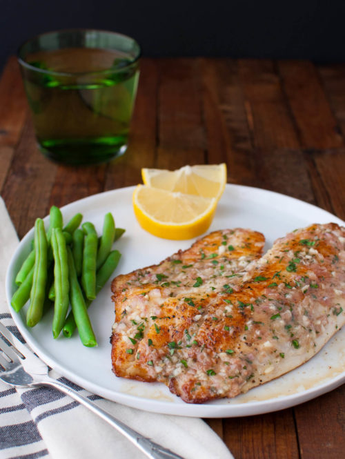 Sautéed tilapia fillet, green beans, and lemon wedges on a white plate.