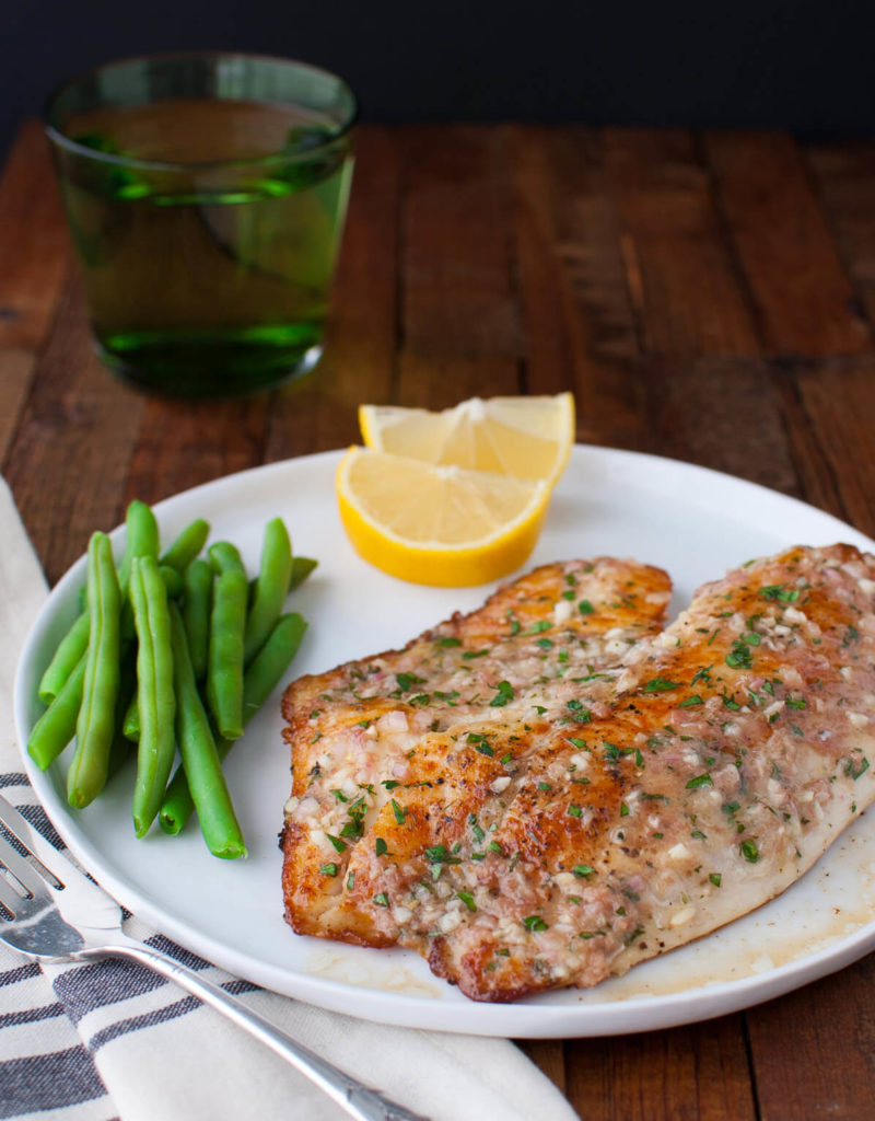 Sautéed tilapia fillet, green beans, and lemon wedges on a white plate.